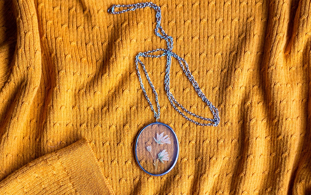 Exemplo de joias e bijuterias feitas em resina: um colar com pendente em resina rosa com flores no interior, em cima de uma blusa de lã amarela.